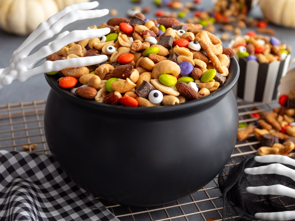 Halloween Monster Munch Trail Mix with skeleton hand serving utensils in a caldron bowl