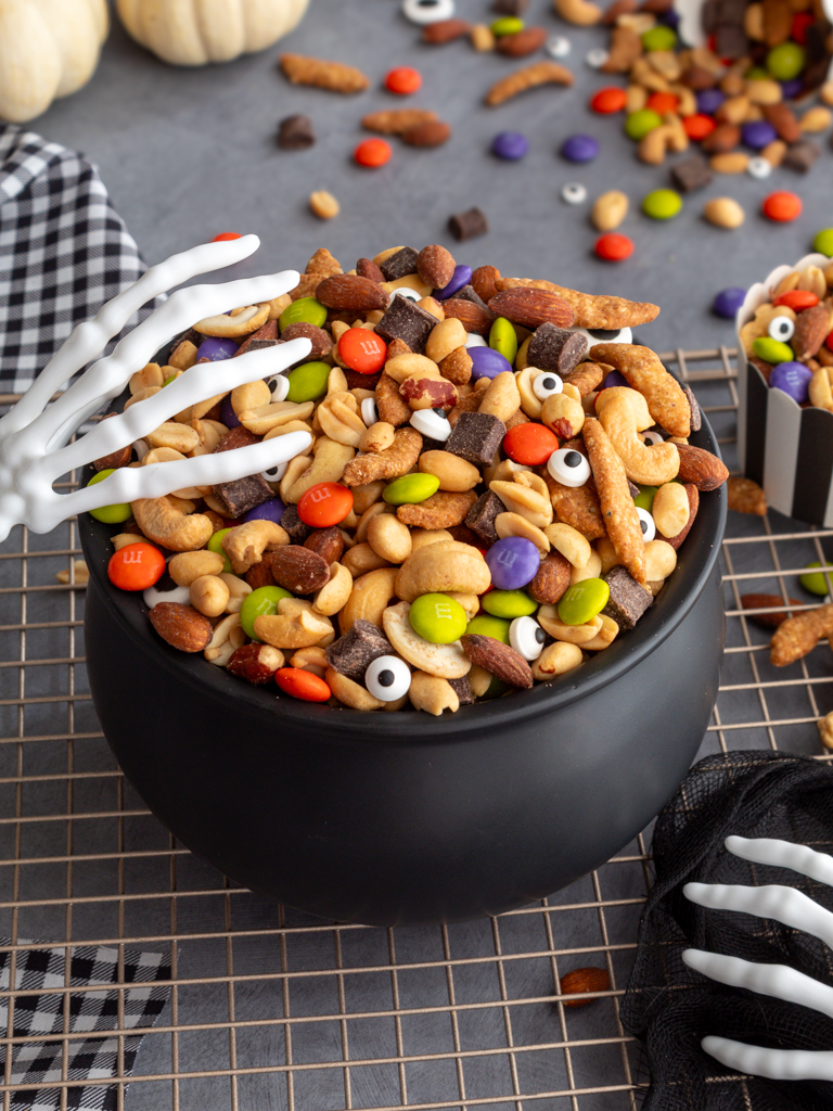 Halloween Monster Munch Trail Mix with skeleton hand serving utensils in a caldron bowl on top of a baking rack