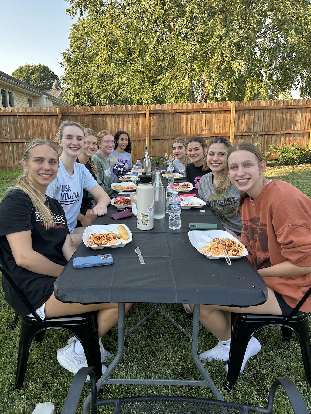 High school volleyball team eating spagehetti for a team dinner in the back yard. 