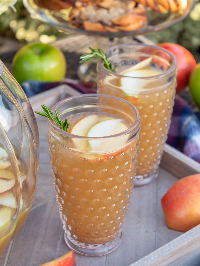 Overhead view of glasses fo caramel apple sangria garnished with extra apple slices and fresh sprigs for rosemary