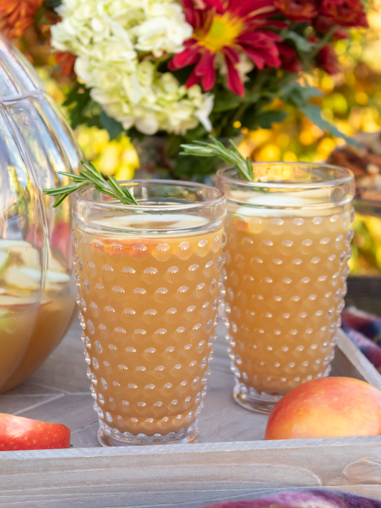 Up close view of hobnail glasses filled with fall caramel apple sangria with white wine and caramel flavored vodka served on a wooden farmhouse tray