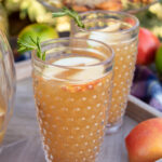 Two glasses of caramel aplple sangria on a wooden serving tray with springs for fresh rosemary garnish