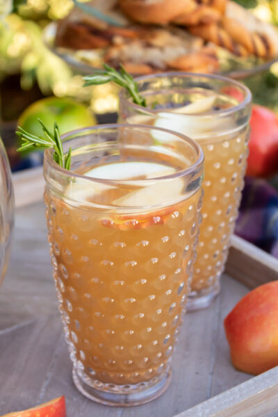 Two glasses of caramel aplple sangria on a wooden serving tray with springs for fresh rosemary garnish