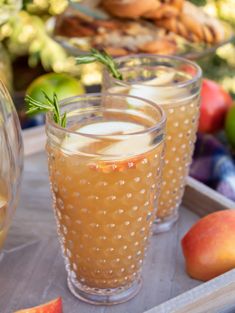 Two glasses of caramel aplple sangria  on a wooden serving tray with springs for fresh rosemary garnish