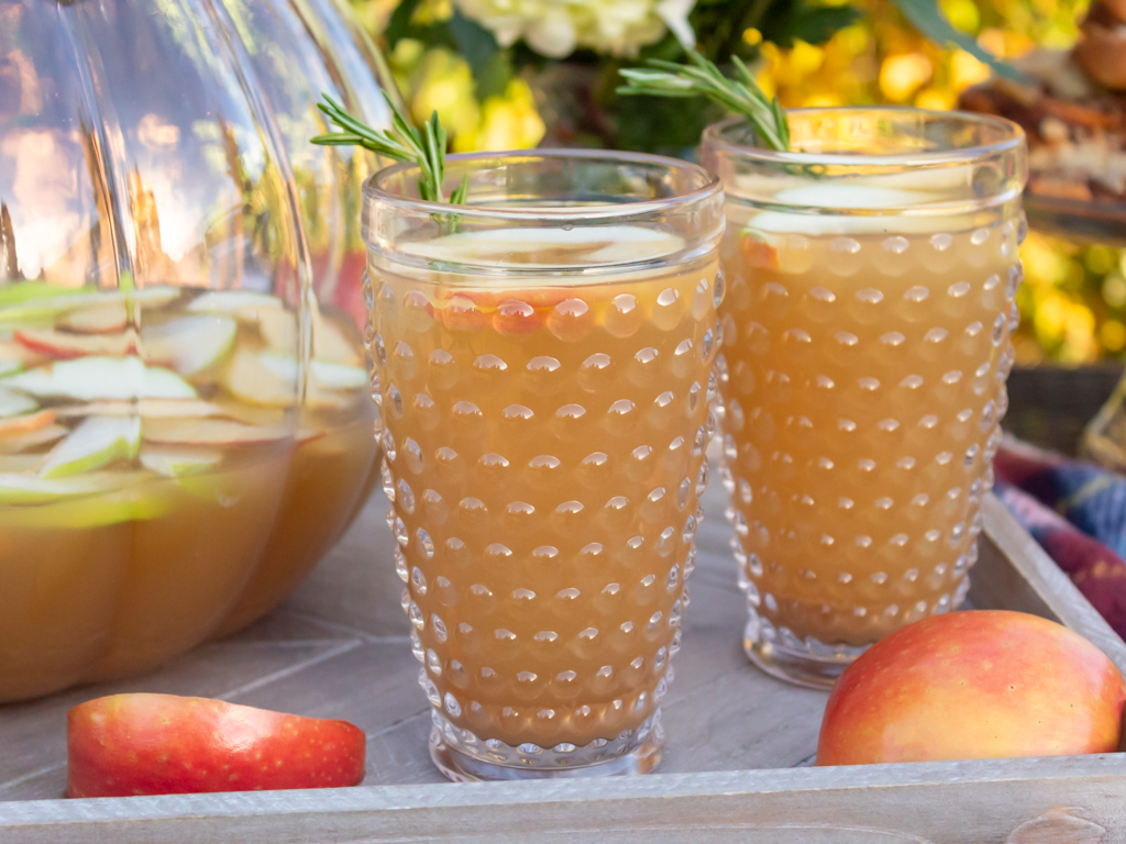 Up close view of hobnail glasses filled with fall caramel apple sangria with white wine and caramel flavored vodka served on a wooden farmhouse tray