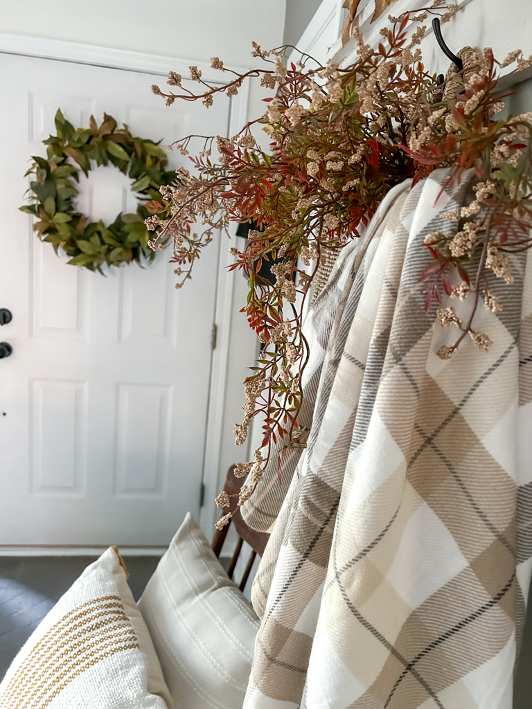 Entry decoratd for fall with a basket hangining on a shelf filled with a plaid blanket and fall foliage