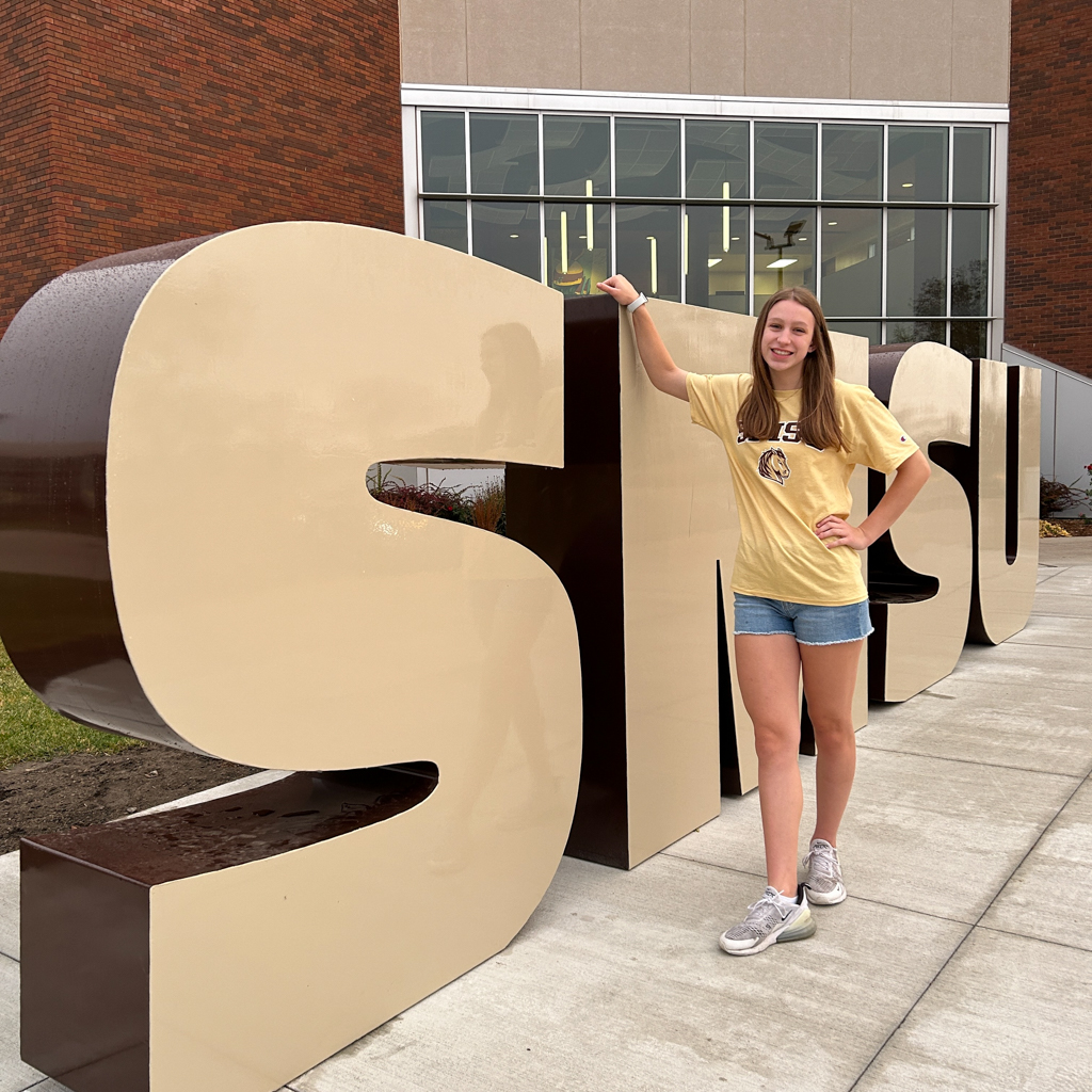 student posing in front of large SMSU letters on their college campus near the visitor's center