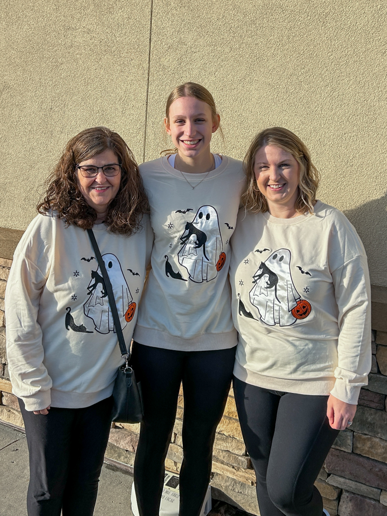 mom, daughter, and granddaugther smiling and wearing matching Halloween sweatshirts 