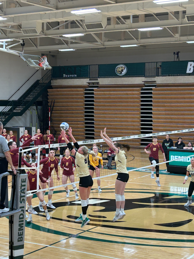 photos from a college volleyball game of a girl attacking the ball and two other girls goign up for a block