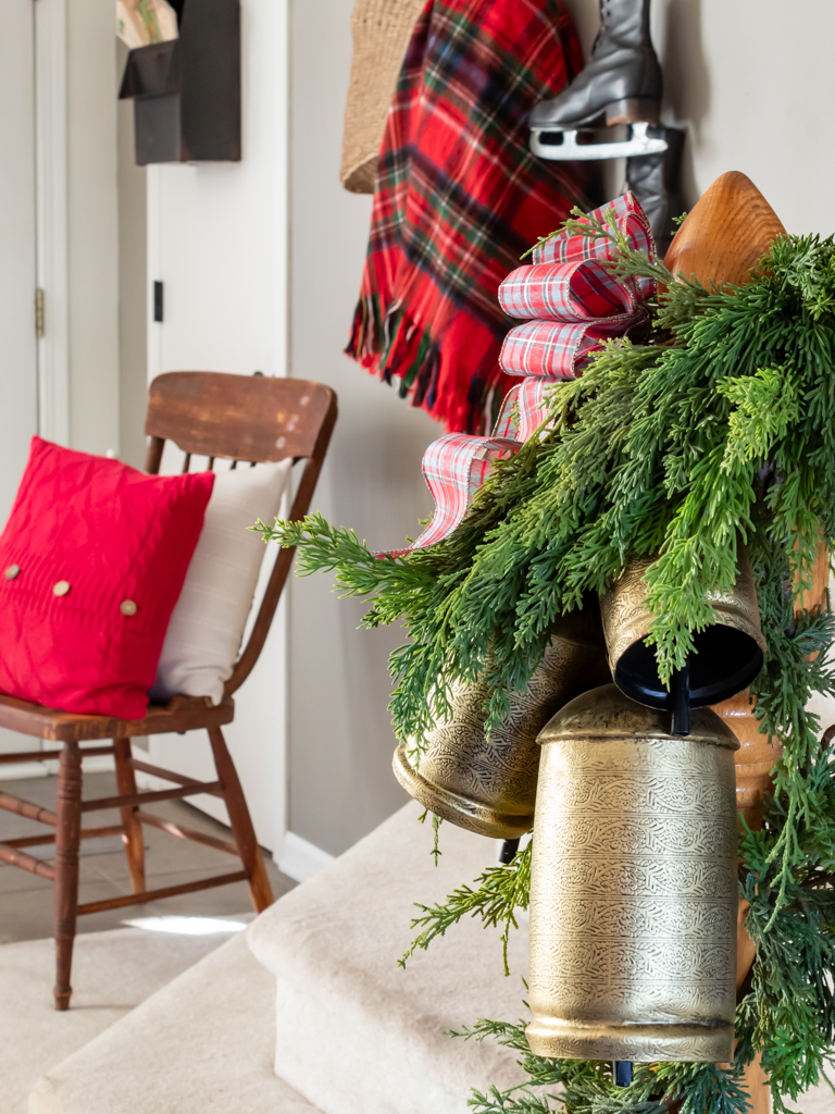 Railing deocrated with Christmas greenery, a set of three gold bells and a plaid bow