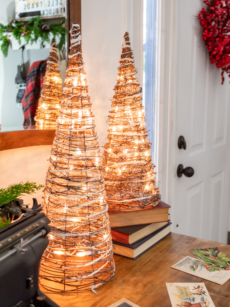 Vintage dresser in the dining room decorated with a christmas vignette with some light-up cone Christmas trees sitting on a stack of red and blue vintage books and some antique postcards scattered on top of the dresser