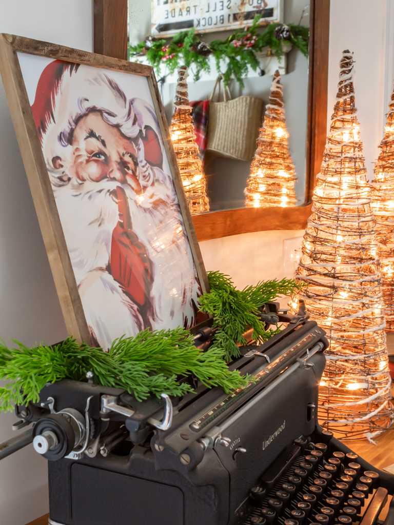 Vintage dresser in the dining room decorated with a christmas vignette including an old typewriter with a framed Santa print sitting on top, some light-up cone Christmas trees