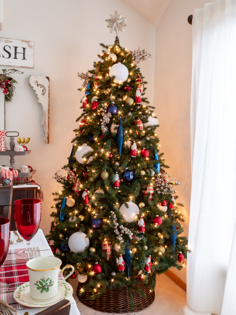 Large Christmas tree in the dining room decorated with red, white, and blue ornaments with a woven tree collar