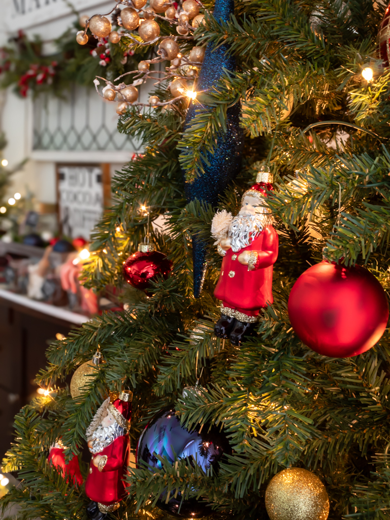 Close up view of a Christmas tree in the dining room decorated with red, white, and navy blue ornaments and vintage looking Santa ornaments