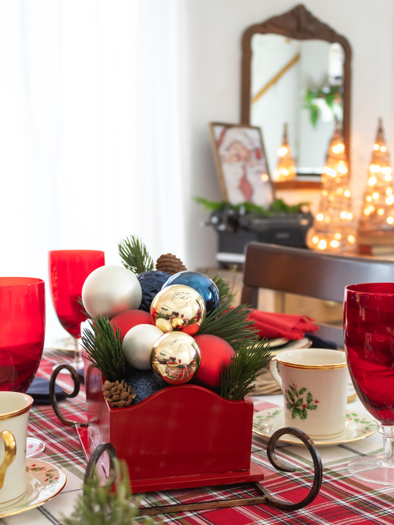 DIY red Santa sleigh Christmas centerpiece set on a holiday tablescape filled with red, gold, white and blue ornaments and greenery