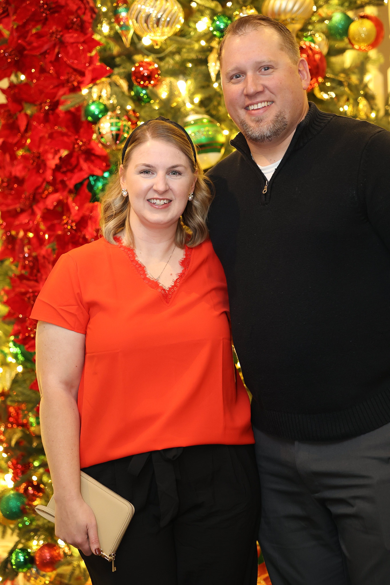 Husband and wife dressed up for Christmas standing in front of a tree at a holiday party