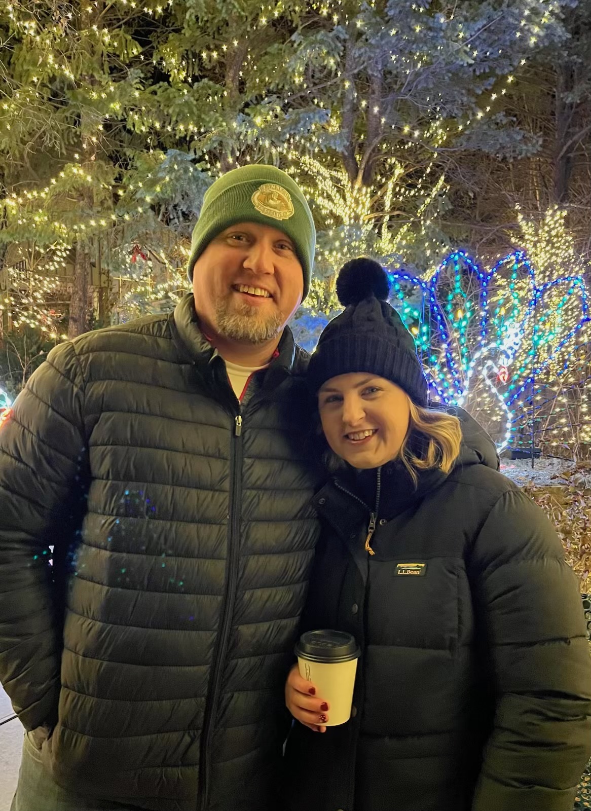 Husband and wife posing outdoors at a zoo lights event