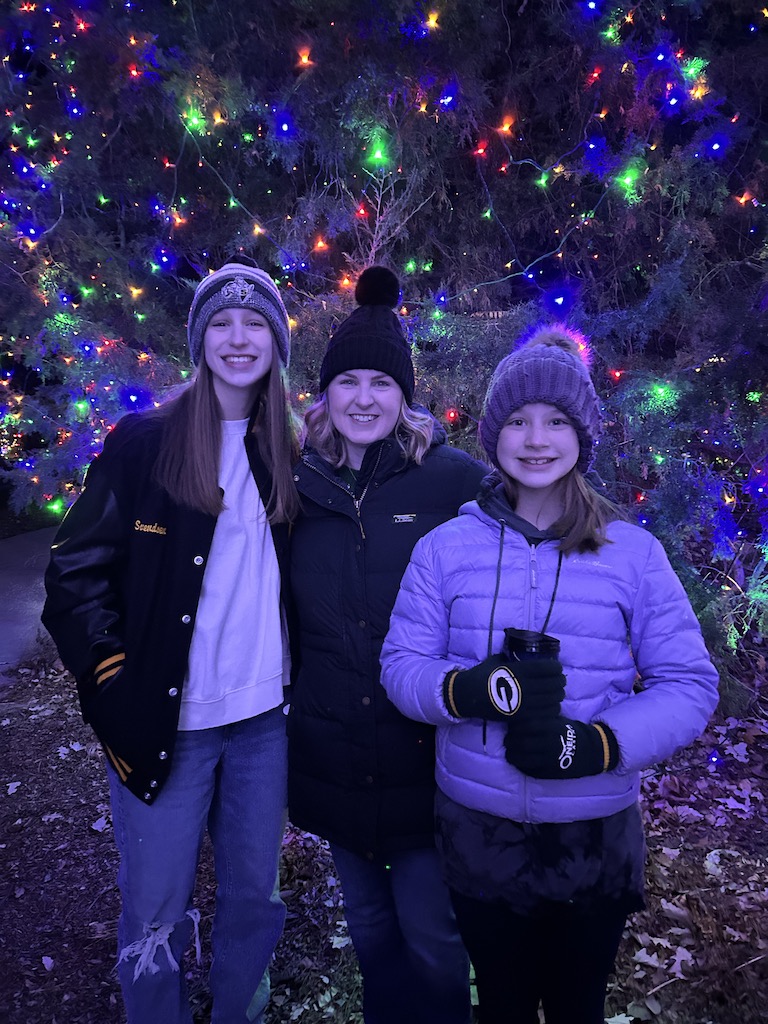 Mother and daughters posing in front of a lit-up Christmas tree outdoors