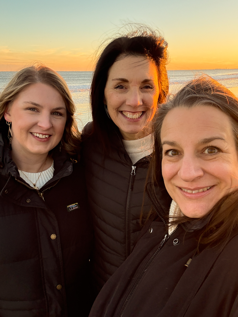 3 women smiling and standing on the beach in the winter