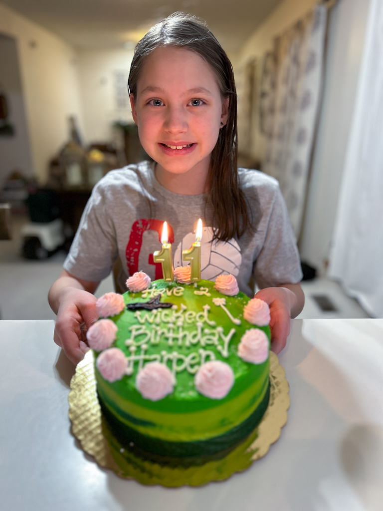 Girl smiling and holding a wicked themed birthday cake. 