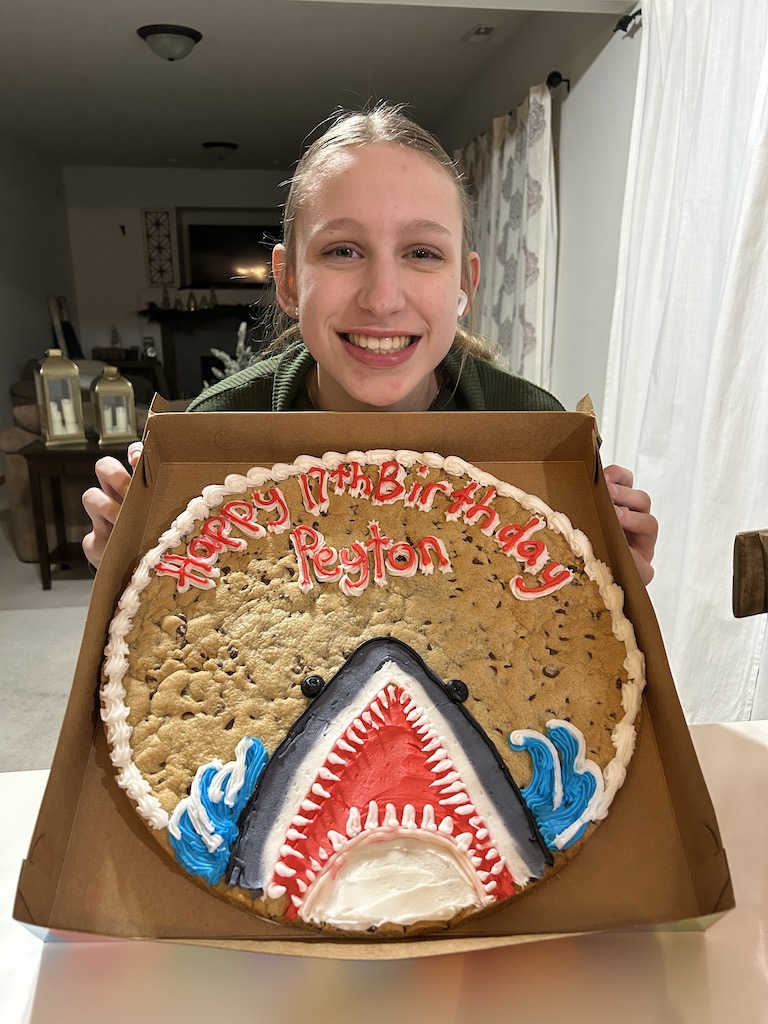 Girl smiling holiding cookie cake for birthday with shark frosted on the cookie