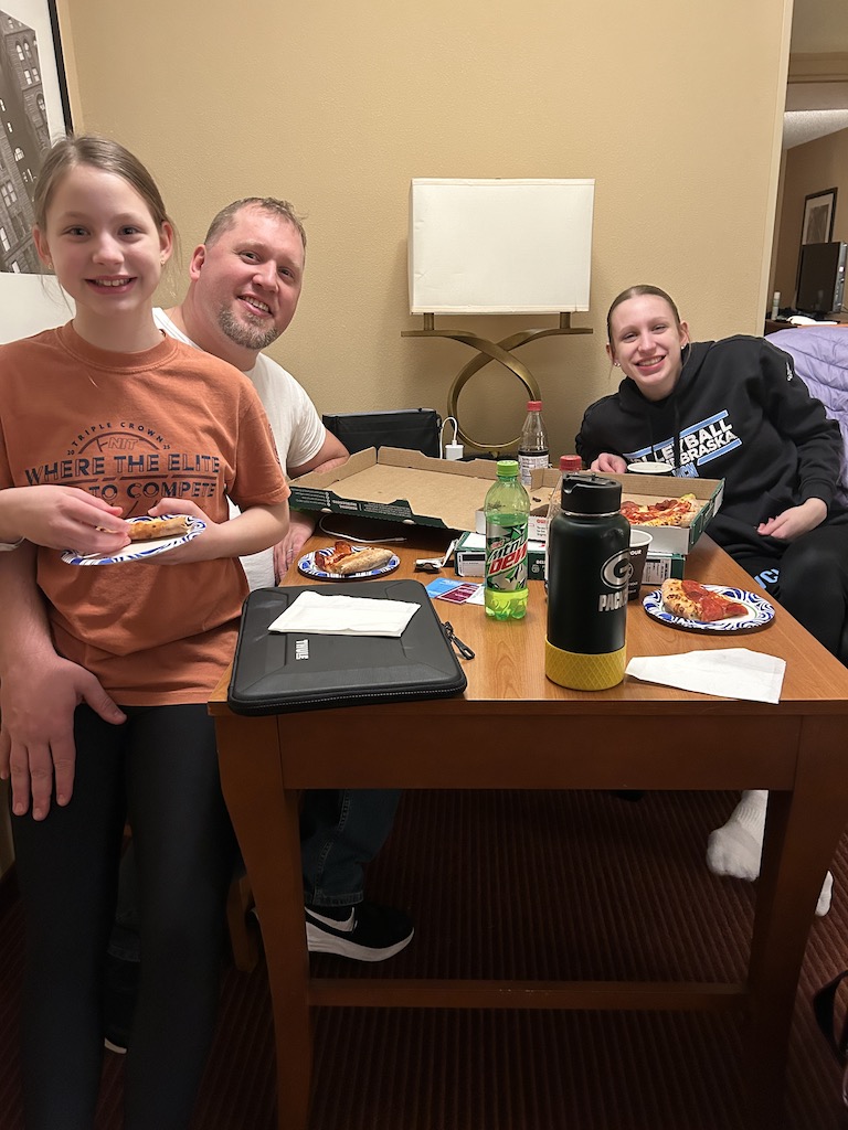 Family eating pizza in a hotel room during a volleyball tournament