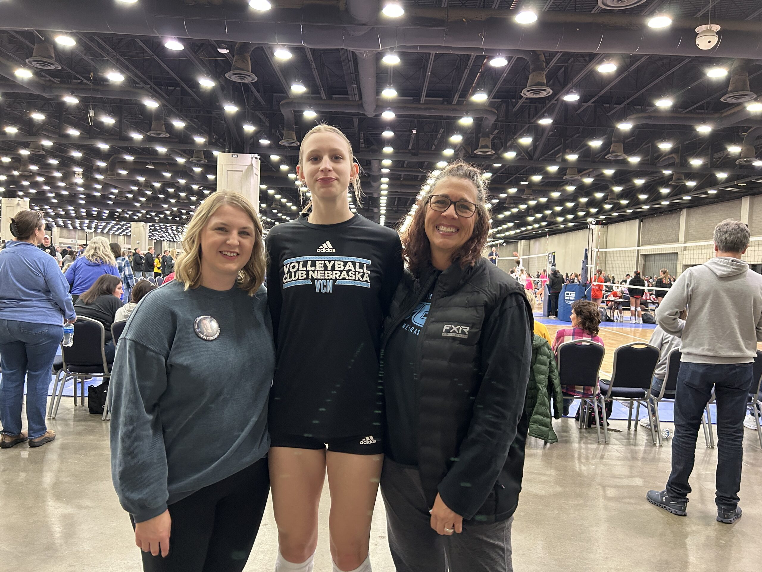 Mom and Grandma standing and smiling with volleyball player at a tournament